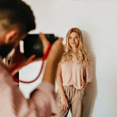 Fotograf robi zdjęcie uśmiechniętej blondynce na białym tle.