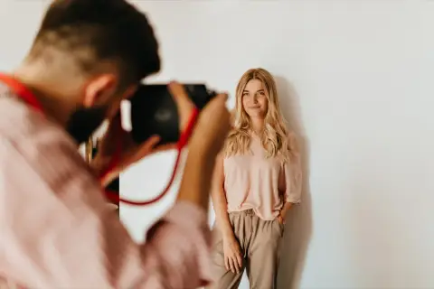 Fotograf robi zdjęcie uśmiechniętej blondynce na białym tle.