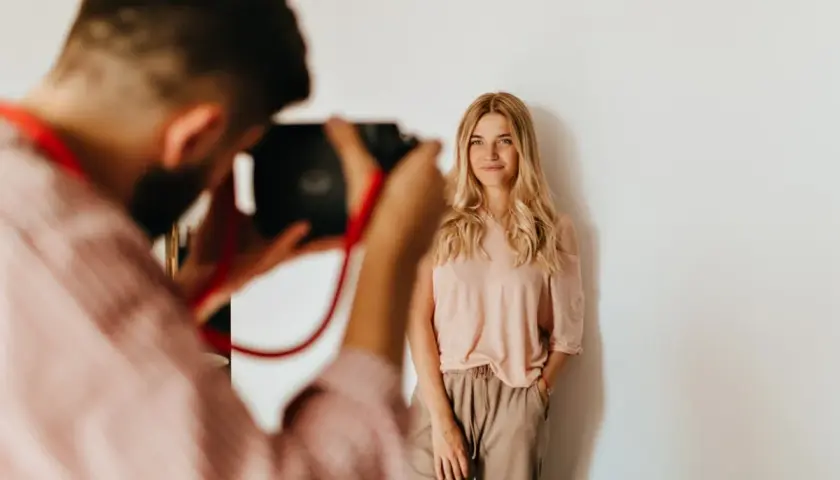 Fotograf robi zdjęcie uśmiechniętej blondynce na białym tle.